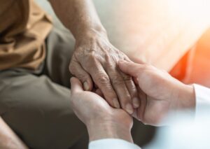 health provider gently holds the hand of an elderly man of color