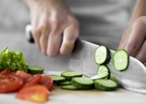 person slices cucumbers and vegetables to make a salad and eat more healthy