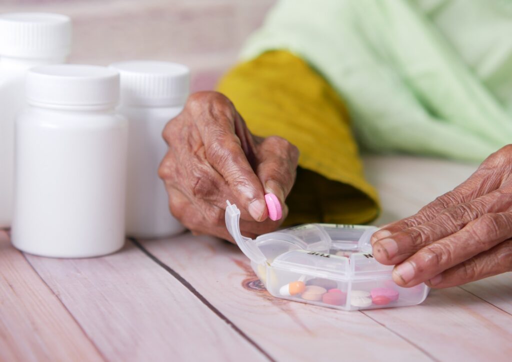 elderly woman of color takes a pill out of a weekly medication container