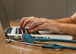 woman with stethoscope on a desk types on a laptop