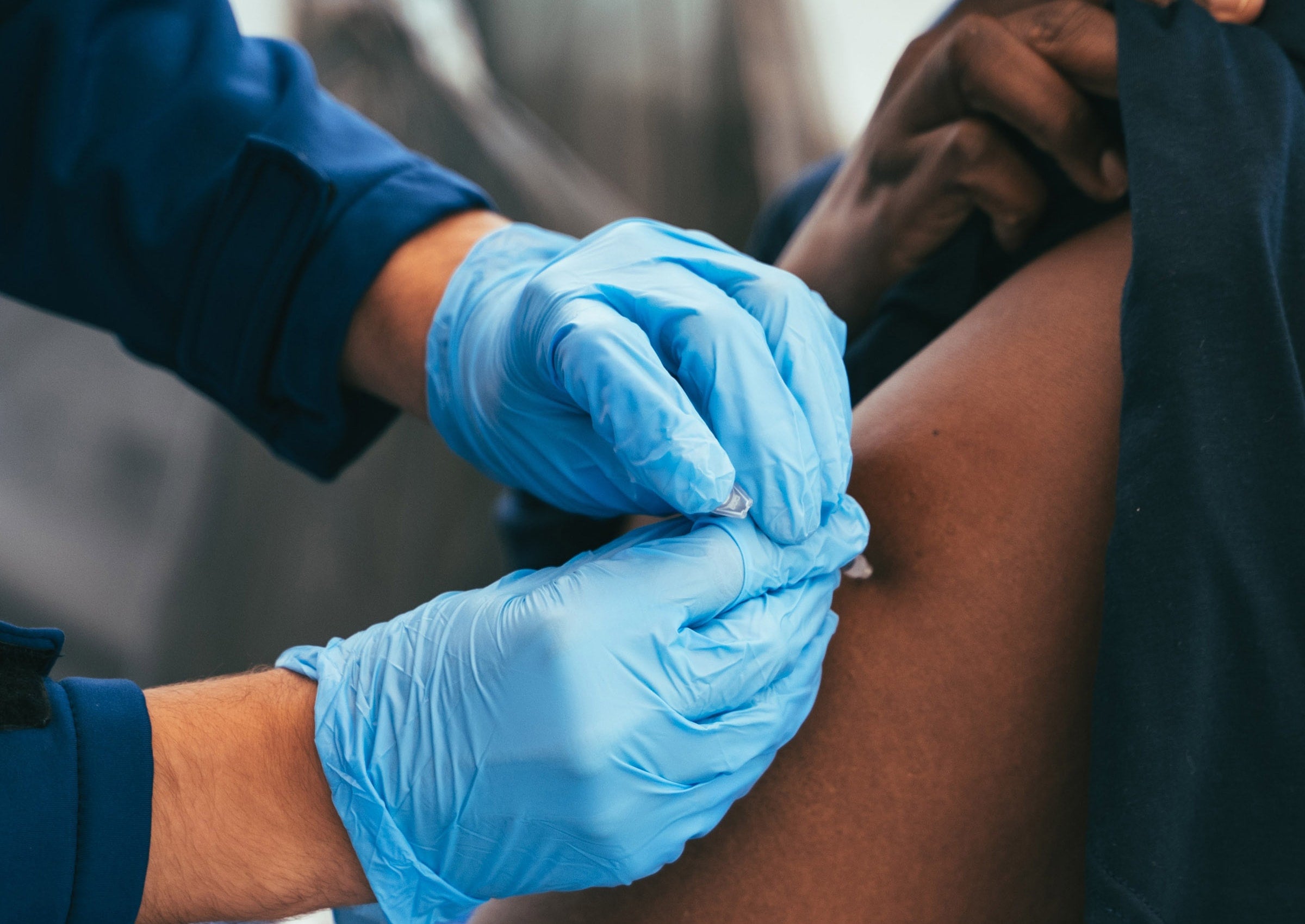 nurse wearing blue medical gloves administers a vaccine to a person in their arm