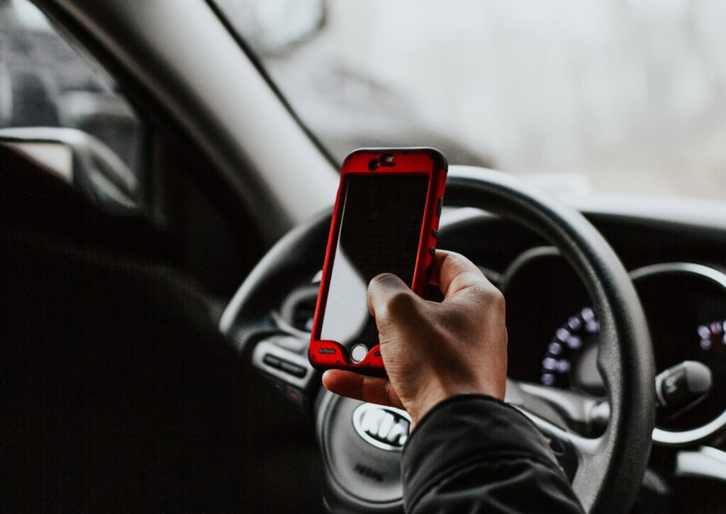 person holding cell phone and steering wheel to demonstrate distracted driving