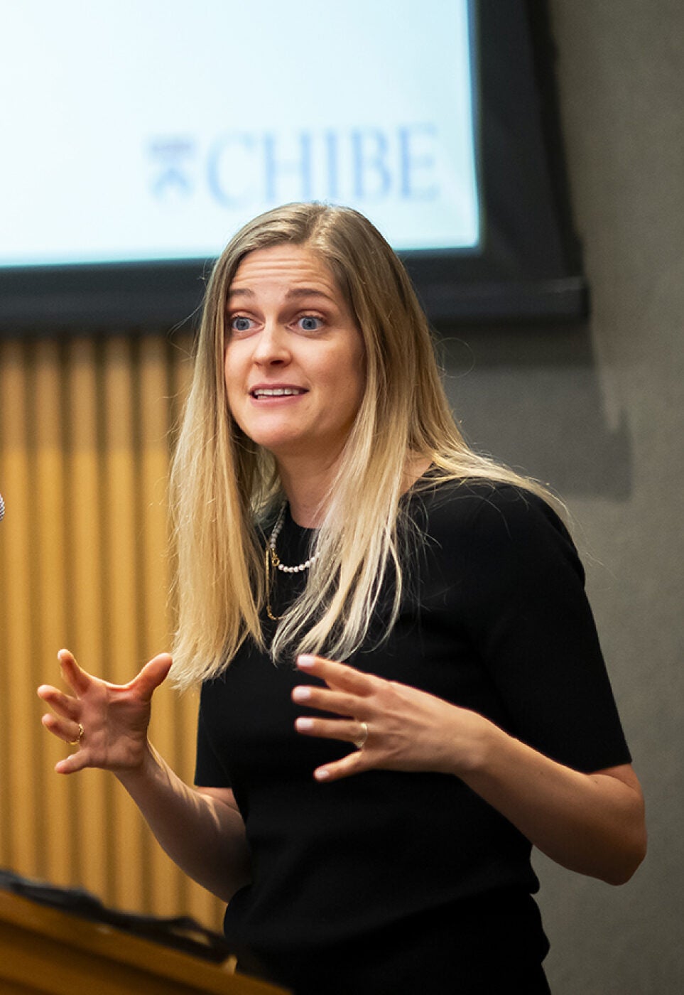 Woman giving a talk at a podium, CHIBE logo visible on the display screen in the background