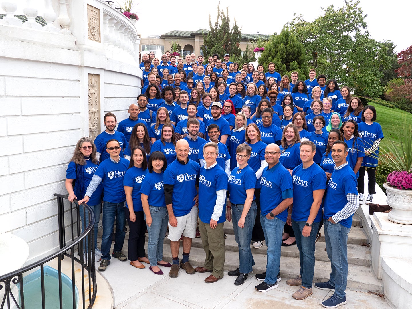 Group photo of CHIBE members at a retreat posing outdoors while wearing blue shirts with the Penn logo